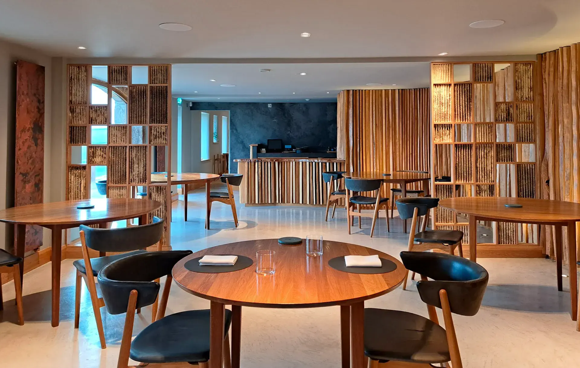 Warm restaurant dining room with timber-framed mycelium panels, set tables, and leather chairs
