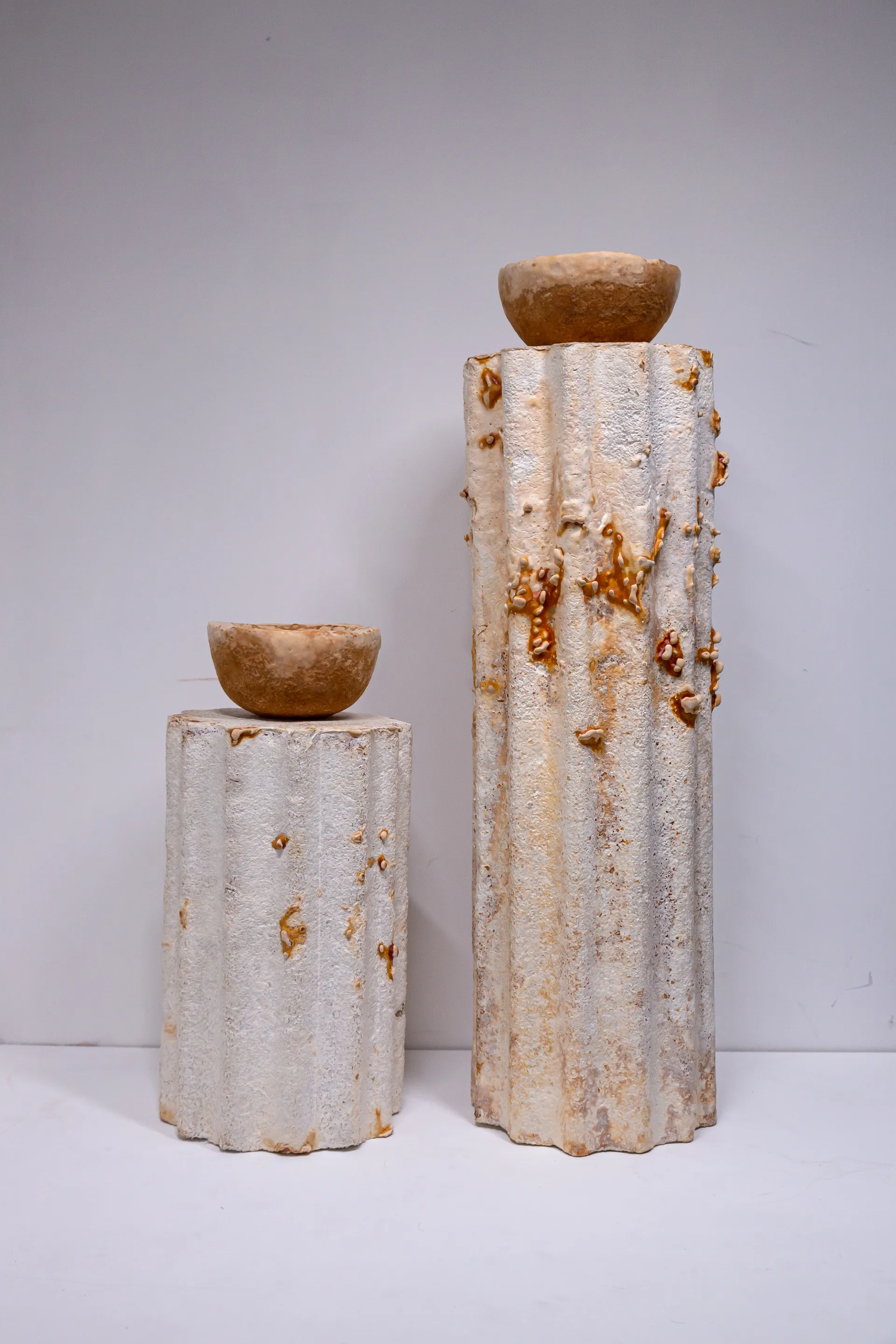 Two tall mycelium plinths with sculptural grown forms against a soft lavender backdrop